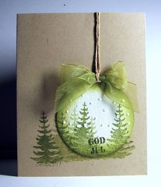 a green ornament hanging from a string on top of a card with trees