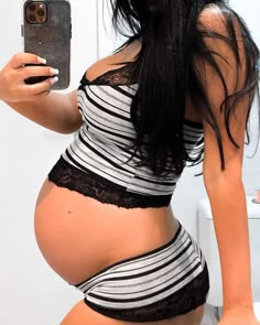 a pregnant woman taking a selfie in the bathroom with her cell phone while wearing a black and white striped bathing suit