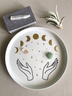 a white plate with two hands holding the moon and stars on it next to an air plant