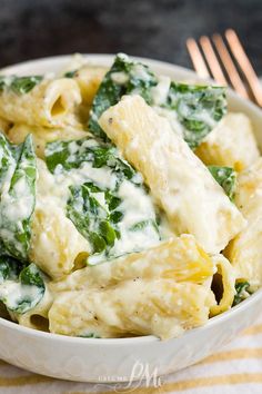 a white bowl filled with pasta and spinach covered in sauce next to a fork