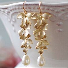 gold earrings with flowers and pearls hanging from the end of each earring, on a white cup