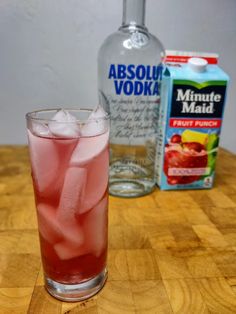 a glass filled with ice sitting on top of a wooden table next to a bottle