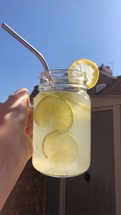 a person holding up a mason jar with lemon and limes on the rim, in front of a house