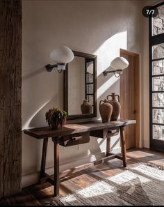 a wooden table with two vases on top of it next to a mirror and lamp