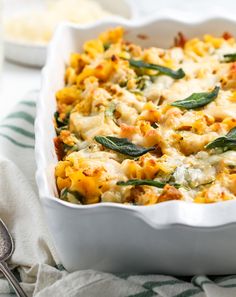 a casserole dish filled with pasta, cheese and spinach garnished with sage