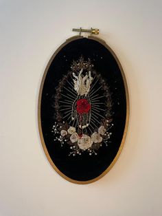 a black and gold embroidered wall hanging on a white wall with flowers in the center