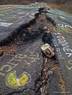 the road has been vandalized with graffiti on it and is cracked into pieces