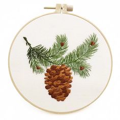 a pine cone and branch embroidered onto a white hoop