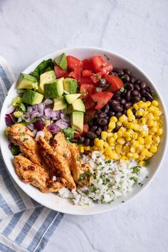 a white bowl filled with chicken, rice and veggies next to a fork