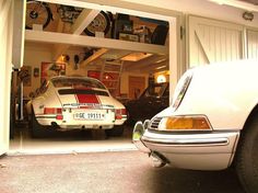 two cars parked in front of a garage with bikes on the wall and one is white