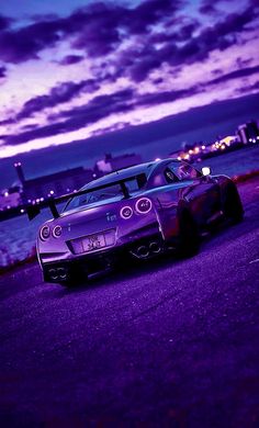 a purple car parked on the side of a road next to some water at night