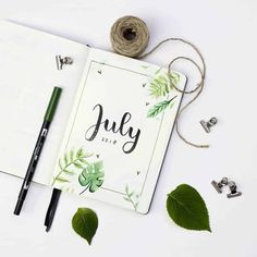 an open notebook with the word july on it next to some green leaves and twine