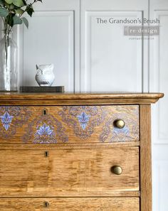 a wooden dresser with blue and white designs on the drawers, next to a vase filled with flowers