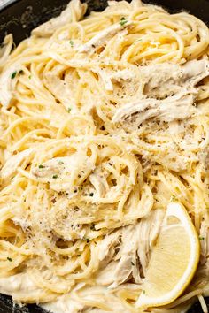 chicken alfredo in a skillet with lemon wedges