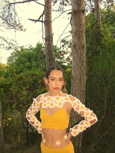 a woman standing in front of some trees wearing a crop top and yellow skirt with flowers on it