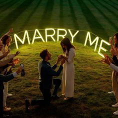 a group of people standing around each other in front of a sign that says marry me