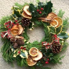 a christmas wreath with oranges, holly and pine cones on it sitting on the ground