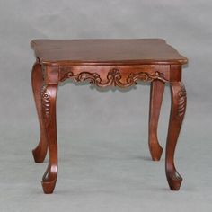 a small wooden table with carvings on the top and bottom legs, sitting against a gray background