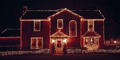 a red house with christmas lights on it's windows and front door at night