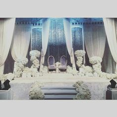 an elaborately decorated stage with chairs and flowers on the side, surrounded by white drapes