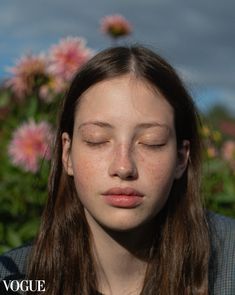 a girl with freckled hair and eyes closed is in front of pink flowers