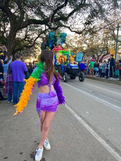 a woman in a purple and yellow costume walking down the street with people watching her