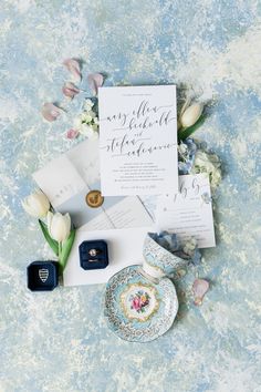 wedding stationery with calligraphy and flowers laid out on a blue floraled background