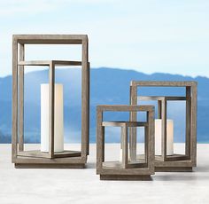 three square and rectangular candle holders sitting on top of a cement surface with mountains in the background