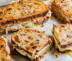 several grilled sandwiches sitting on top of a pan covered in melted cheese and meat