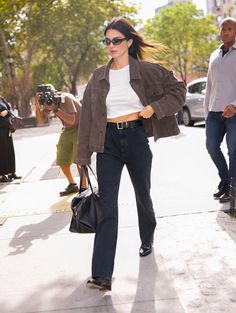 a woman walking down the street with her hair blowing in the wind and wearing sunglasses