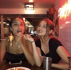 two women sitting at a table with food in their hands and one is eating something