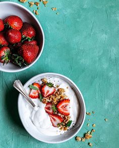 two bowls filled with yogurt and strawberries on top of a green table