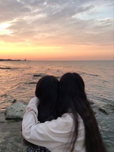 two people embracing each other while standing on rocks near the water at sunset or dawn