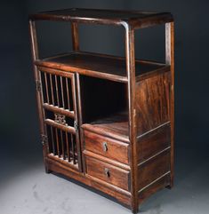 an old wooden cabinet with two drawers and bars on the bottom shelf, against a dark background