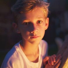 a young boy is looking at the camera while wearing a white t - shirt and holding his hand over his shoulder