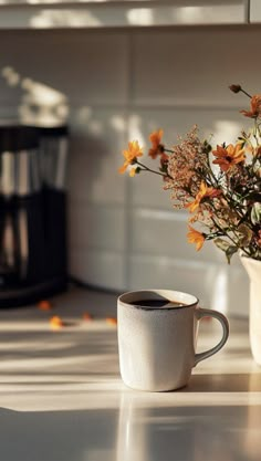 a coffee cup sitting on top of a counter next to a vase filled with flowers