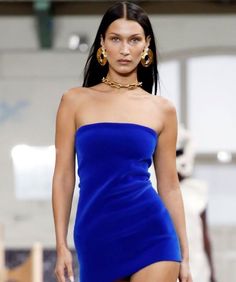 a model walks down the runway wearing a blue dress with high slits and gold hoop earrings