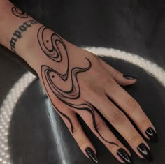 a woman's hand with black nail polish and tattoos on her left arm, sitting on a table