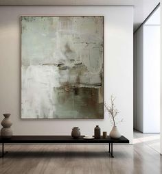 an abstract painting hangs on the wall above a coffee table with vases in front of it