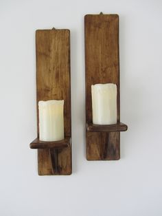 two candle holders made out of wooden planks with white candles in them on the wall