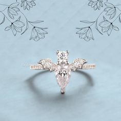 an engagement ring with a pear shaped diamond in the center, surrounded by leaves and flowers