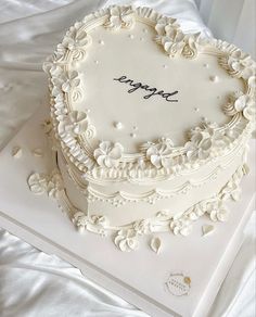 a heart shaped cake with the word happy written on it, sitting on a white tablecloth