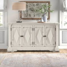 a white dresser with a mirror and lamp on top of it next to a rug