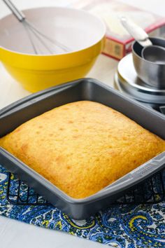 a cake in a pan sitting on top of a blue and white place mat next to a yellow bowl