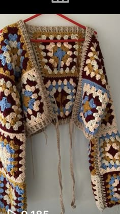 a crocheted jacket hanging on a wall with a red hanger attached to it