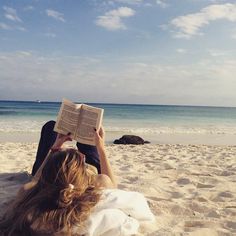 a woman laying on the beach reading a book