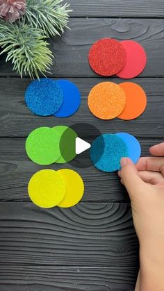 someone is making colorful paper circles with colored sand on the table next to a potted plant