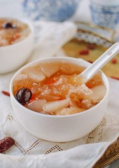 two bowls filled with soup and fruit on top of a cloth covered place mat next to cups