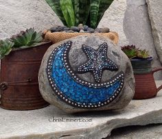 a rock with a star and moon painted on it next to some succulents