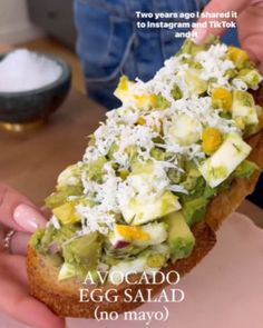 someone holding up a sandwich with avocado and other toppings